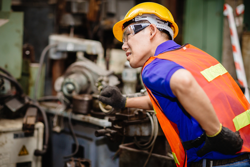 Construction worker holding his back in pain while handling machinery