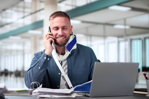 In Need of Workers' Compensation Lawyer in Las Vegas Nevada Man talking on the phone while looking at his laptop with a neck and arm cast on