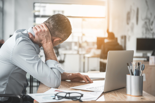 Man holding his neck in pain sitting in front of a laptop