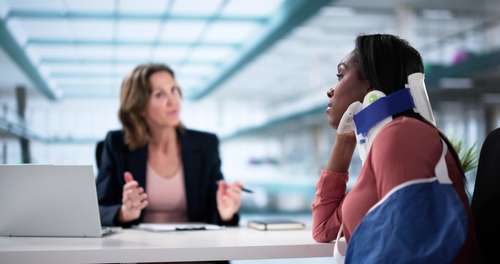 Woman wearing an arm sling and neck brace talking with a lawyer about workers' comp