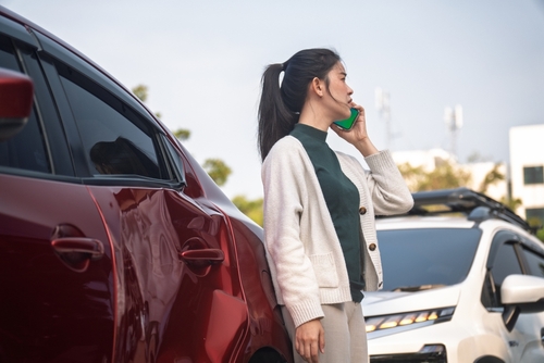 Woman After Car Accident in Albuquerque New Mexico Young woman sitting beside damaged car after collision, holding arm near roadway