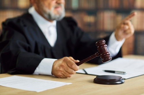 Judge holding gavel above desk with documents and pointing hand in courtroom