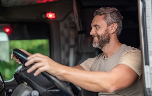 Man driving semi-truck cab with hands on steering wheel