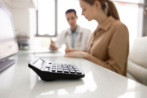 Calculating Medical Bills After Car Accident Jackson MS Calculator on desk with two blurred people seated in office consultation