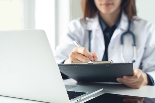 Illinois Doctor Writing Medical Malpractice Certificate of Merit Doctor writing notes on clipboard during patient examination in medical office