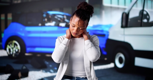 Young woman sitting beside damaged car after collision, speaking on mobile phone