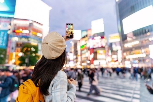 Young woman walking across Shibuya crosswalk with umbrella and shopping bag