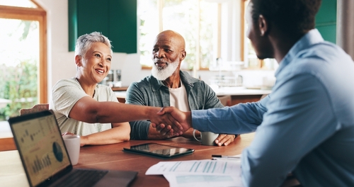 Older couple shaking hands with advisor across table with documents and laptop