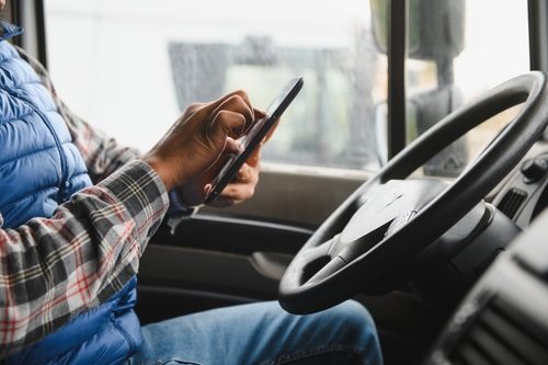 Distracted Commercial Driver Behind Wheel Liberty Missouri Driver using smartphone beside steering wheel inside large commercial vehicle cab