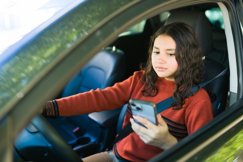 Missouri Teen Driver Safety Risk 2025 Teen driver looking at smartphone while holding steering wheel inside moving car
