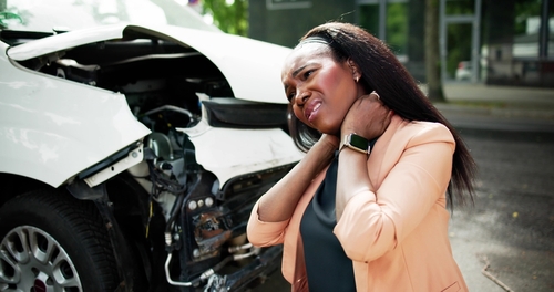 Woman clutching neck beside damaged car after collision, illustrating whiplash injury aftermath