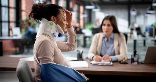Philadelphia Workers Compensation Lawyer Securing Injured Worker Benefits Woman wearing neck brace and arm sling meeting with attorney at desk