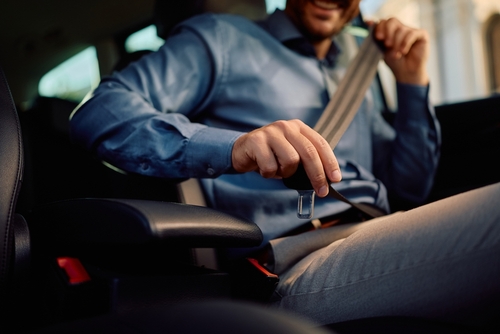 Businessman fastening seat belt inside vehicle, close-up view of torso and hands