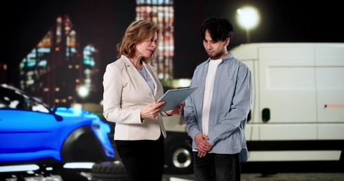 Woman holding clipboard speaks with man beside damaged car and van