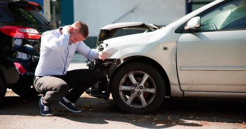 Brooklyn Car Crash Claim Serious Injury Compensation Man crouching beside damaged car front after collision with another vehicle