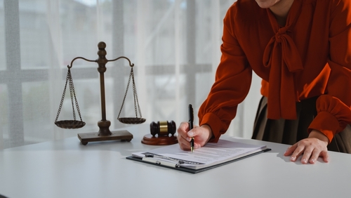 Attorney signing legal document beside scales of justice and gavel on desk