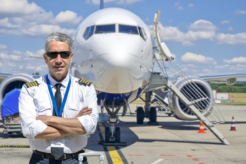 Airline pilot in uniform with arms crossed against aircraft background