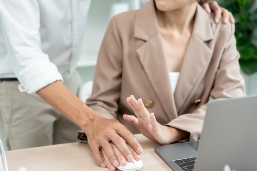 Workplace Sexual Harassment Incident Los Angeles Male manager touching seated female employee while reviewing document in office