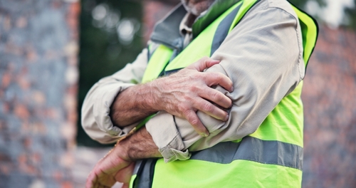 Philadelphia Construction Worker Elbow Pain Work Injury Construction worker in safety vest gripping elbow with both hands outdoors
