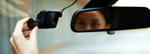 Woman adjusting dashboard camera inside car near rearview mirror