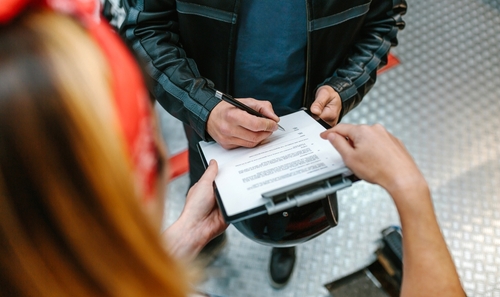 Unrecognizable female mechanic writing on clipboard beside raised vehicle wheel