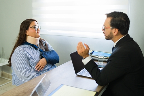 Woman wearing neck brace speaks with attorney across desk in law office