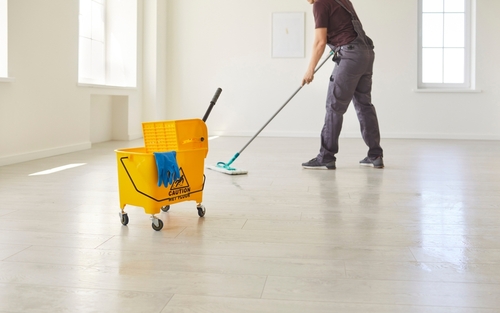 Male janitor in uniform washing floor with mop and cleaning bucket