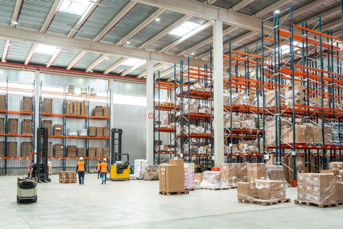 Warehouse workers using tablet and clipboard beside stacked boxes and pallet racks
