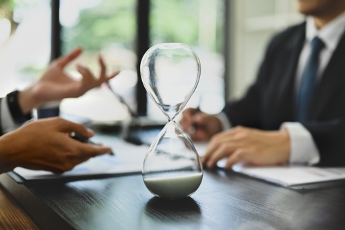 Hourglass on meeting table beside laptop and eyeglasses in office setting