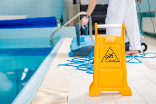 Person cleaning swimming pool with net beside wristwatch on pool edge
