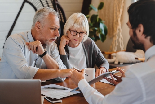 Investors Consulting Securities Fraud Lawyer USA Older couple reviewing paperwork with adviser at table, pen, tablet, and coffee cup