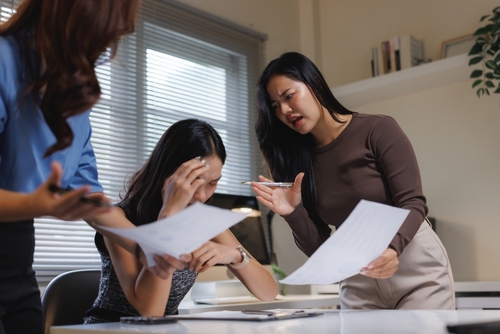 Quid Pro Quo Workplace Harassment Redondo Beach California Three businesswomen holding documents during tense office discussion, one seated with hand on forehead