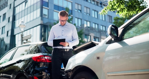 Insurance Agent Assessing Government Vehicle Crash Damage Sacramento Man with clipboard inspecting front-end damage between two cars after collision