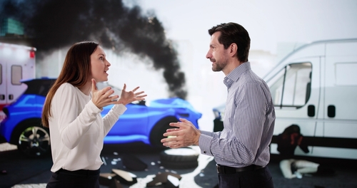 Young man and woman arguing beside damaged car after traffic collision