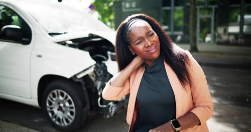 Whiplash Neck Injury After Dayton Car Accident Woman holding neck beside damaged car after traffic collision