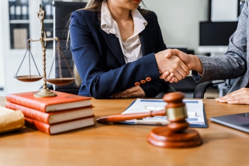USA Shareholder Derivative Suit Lawyers Discussing Case Woman in business suit shaking hands across desk with gavel, scales, and legal documents