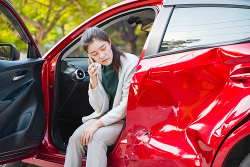 Nebraska Car Accident Crash Insurance Fault Claim Woman sitting in damaged car doorway speaking on phone after collision