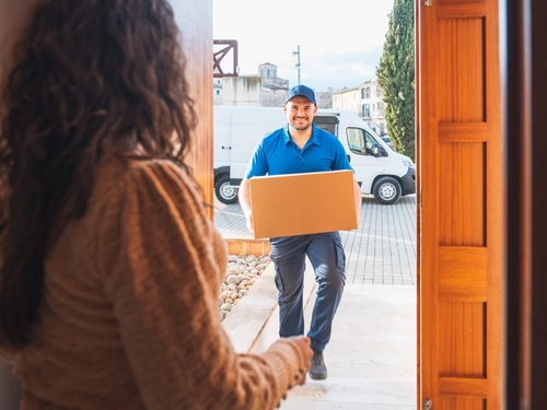 Boston Delivery Driver Handing Package to Customer Delivery driver carrying cardboard package to front door with van parked outside