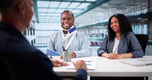Man wearing neck brace and arm sling meeting with woman at office desk