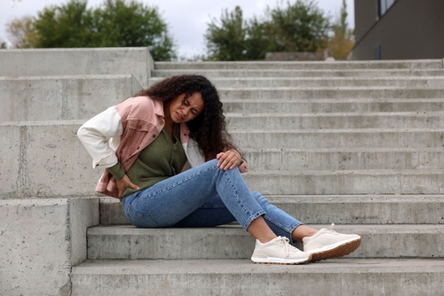 woman sitting on concrete stairs clutching back in visible pain