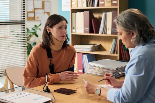 distressed young woman speaking with professional across office desk with documents
