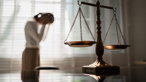 scales of justice in foreground with distressed woman standing in background