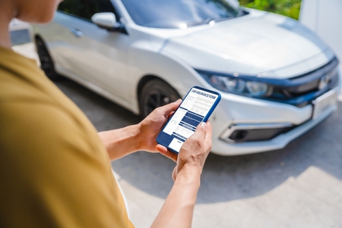 person holding smartphone displaying car insurance form in front of vehicle