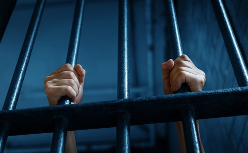 Georgia Felony Conviction Consequences Prison Bars Lawrenceville person's hands gripping metal prison cell bars from behind