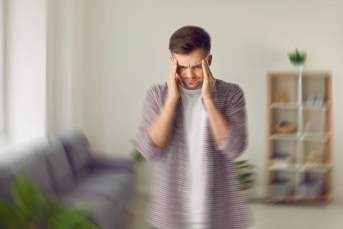 young man pressing temples with both hands appearing dizzy indoors
