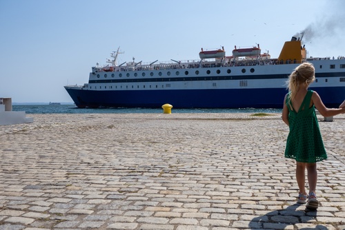 young child standing on cobblestone dock watching large ferry ship at port