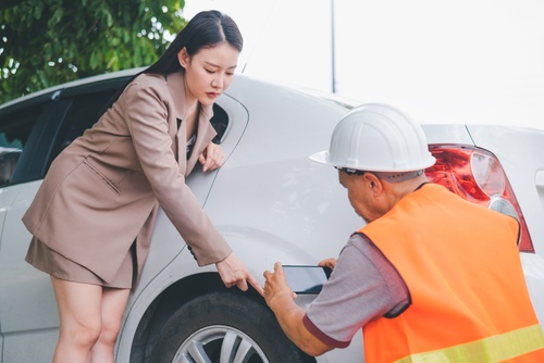 Brooklyn Car Accident Insurance Inspection After Crash insurance inspector with hard hat and tablet examining vehicle damage with woman