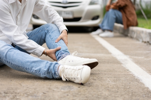 Injured Person After NYC Auto Accident Serious Injury injured person sitting on road gripping leg near vehicles after accident