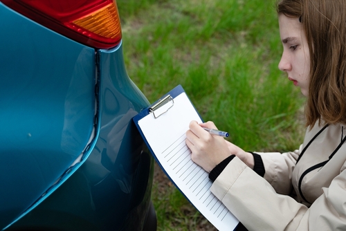 Documenting Car Accident Damage Evidence Charlotte NC insurance agent writing on clipboard while inspecting damaged vehicle bumper