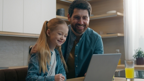 smiling father and young daughter using laptop together in kitchen